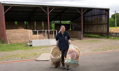 A young woman dragging bags of straw outside a farm building