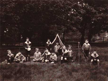 An old black and white photo of a group of boys in scouting uniforms in a field