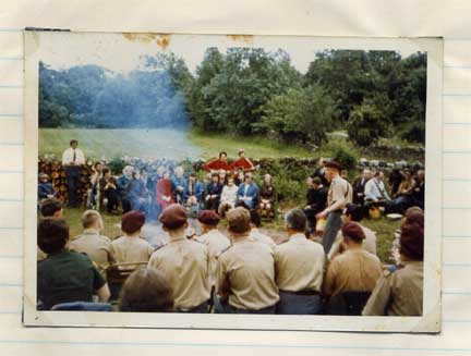An old colour photo of a group of scouts sitting round a camp fire