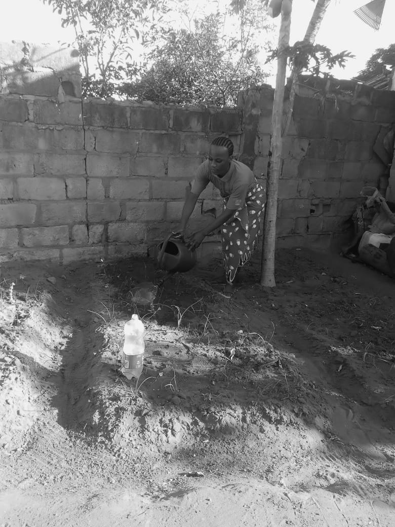 Photo shows a trans woman in Mozambique watering her garden. The image is in black and white