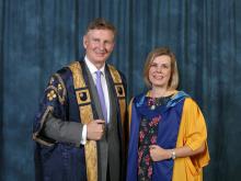 Mr Malcolm Sweeting and Dr Jane Secker are both wearing graduation robes, standing next to each other and smiling at the camera.