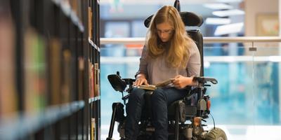 a woman in a wheelchair reading a book in a library