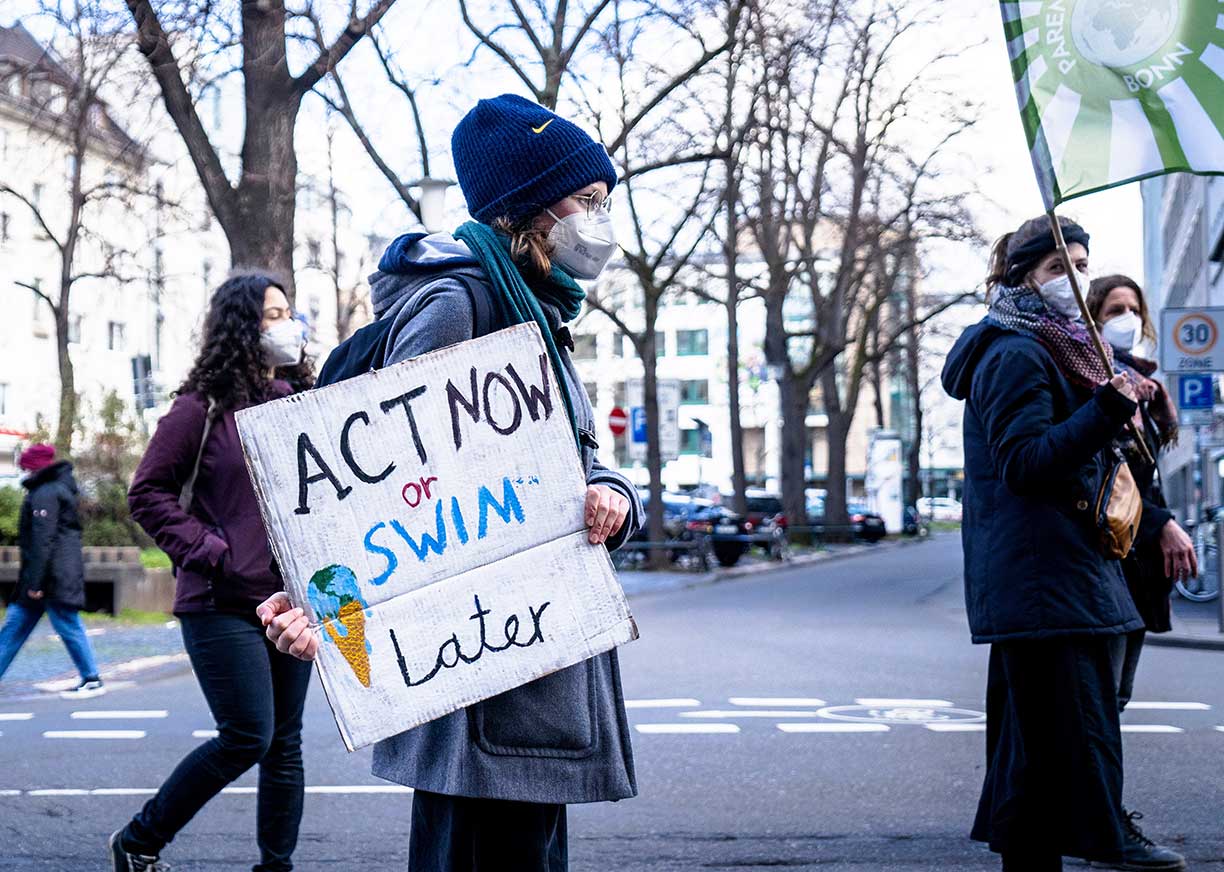 Woman protesting with sign saying 'Act now or Swim later