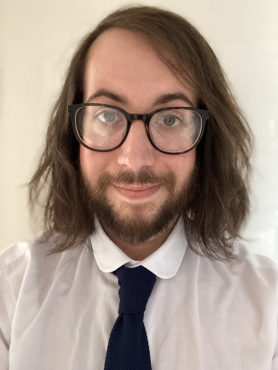 Photograph of Dr George Sandifer-Smith, a white man with dark hair, beard and glasses, wearing a white shirt and knitted navy tie.