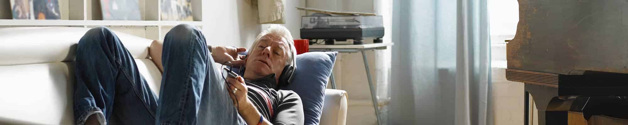 Mature man lying on sofa listening to music