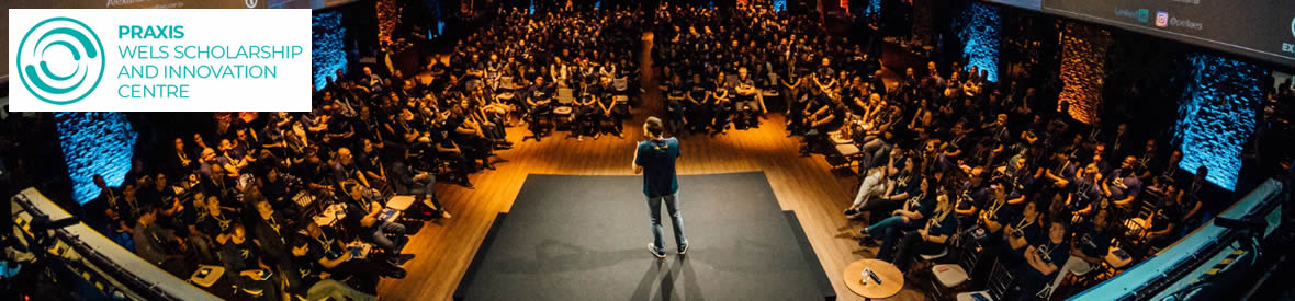 A man on a stage in an auditorium delivering a presentation to a large audience.