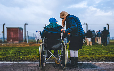 A woman crouching next to a wheelchair user (photo taken from behind them)