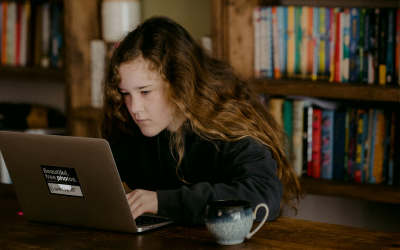 Photo of a young person using a laptop on a dining table, with a mug beside them. 