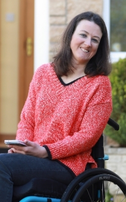 Dr Julie McElroy in garden using wheelchair and holding smart phone