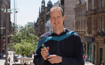 OU graduate Stuart Borland, pictured in Glasgow wearing his graduation gown and holding a scroll. Photo by Mick McGurk.