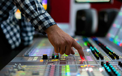 A hand shown over a sound mixing board, with a button about to be pressed