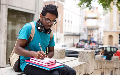 Student outdoors with books and headphones
