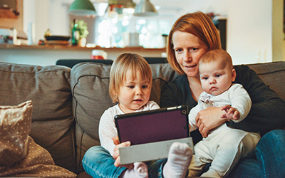 A woman on a sofa with two young children, looking at an iPad