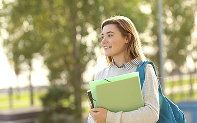 A female student outdoors, holding a notepad and folders