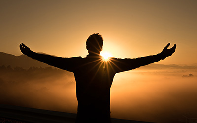 A person with their arms outstretched towards the sun