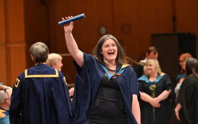 A happy graduate holding an Open University scroll