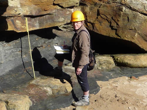 Scientist taking measurements at the base of a rock face