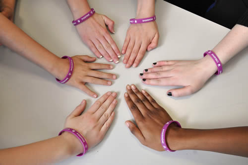 Six people's hands placed on a table forming a circle.