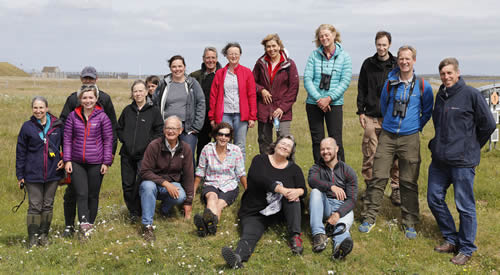 A group of men and women wearing outdoor clothing and standing together in a field