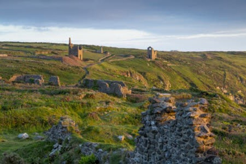 A view of a grassy bank with ruined engine houses, used originally to extract tin from rock along the coastline in Cornwall.