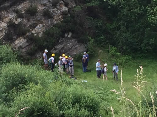Members of a field school in helmets, working at the bottom of a cliff