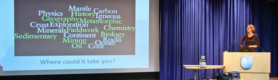 EEES Engagement - a female academic gives a presentation on stage with a large screen showing geology terms