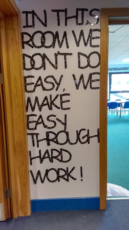 Large sign says 'In this room we dont do easy. We make easy through hard work!'