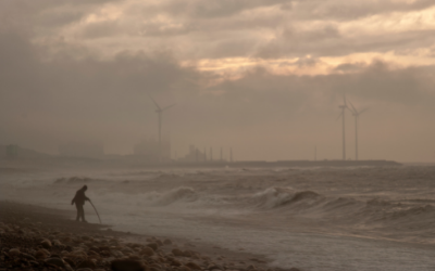 A walker at the beach in front of a rough sea and windfarms
